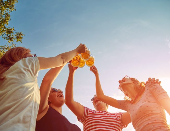 Group of young people enjoying and cheering beer outdoors.